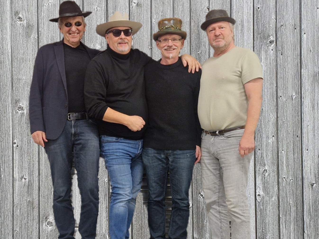 das BBB-Quartett, bestehend aus vier Männern mittleren Alters, posiert vor einer Holzwand. Alle tragen Hüte und Jeans