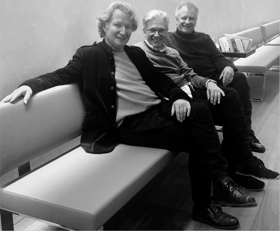 Schwarz-Weiß-Fotografie mit drei lächelnden Männern, die auf einer Bank sitzen.