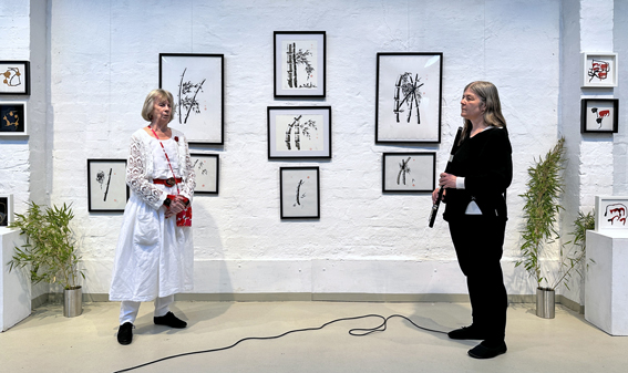 Das Foto zeigt eine musikalische Darbietung von der Künstlerin Lena Römer zusammen mit einer Frau mit Querflöte zur Vernissage der Ausstellung "Ton der Stille"